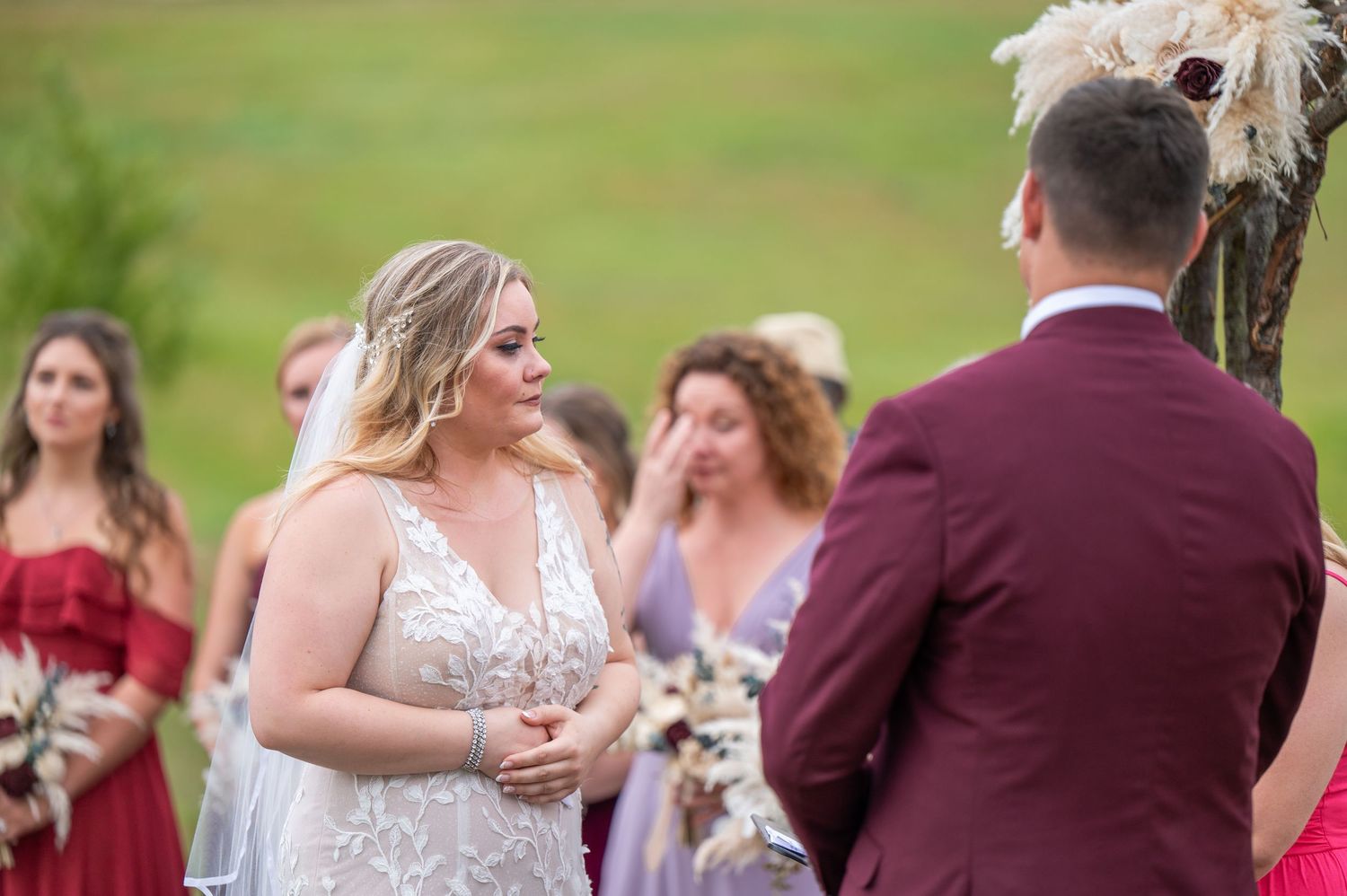 A couple exchanging vows during an outdoor wedding ceremony under a rustic arch with guests looking on.