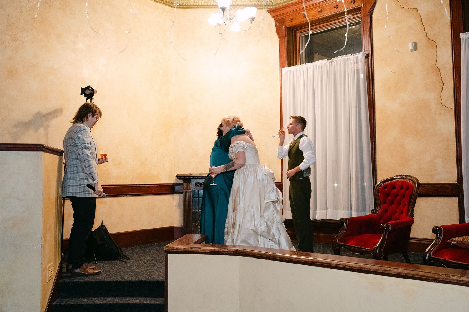 Central MN Wedding Photos | Wedding ceremony with bride in white gown, groom in green vest, and guests in a vintage venue.