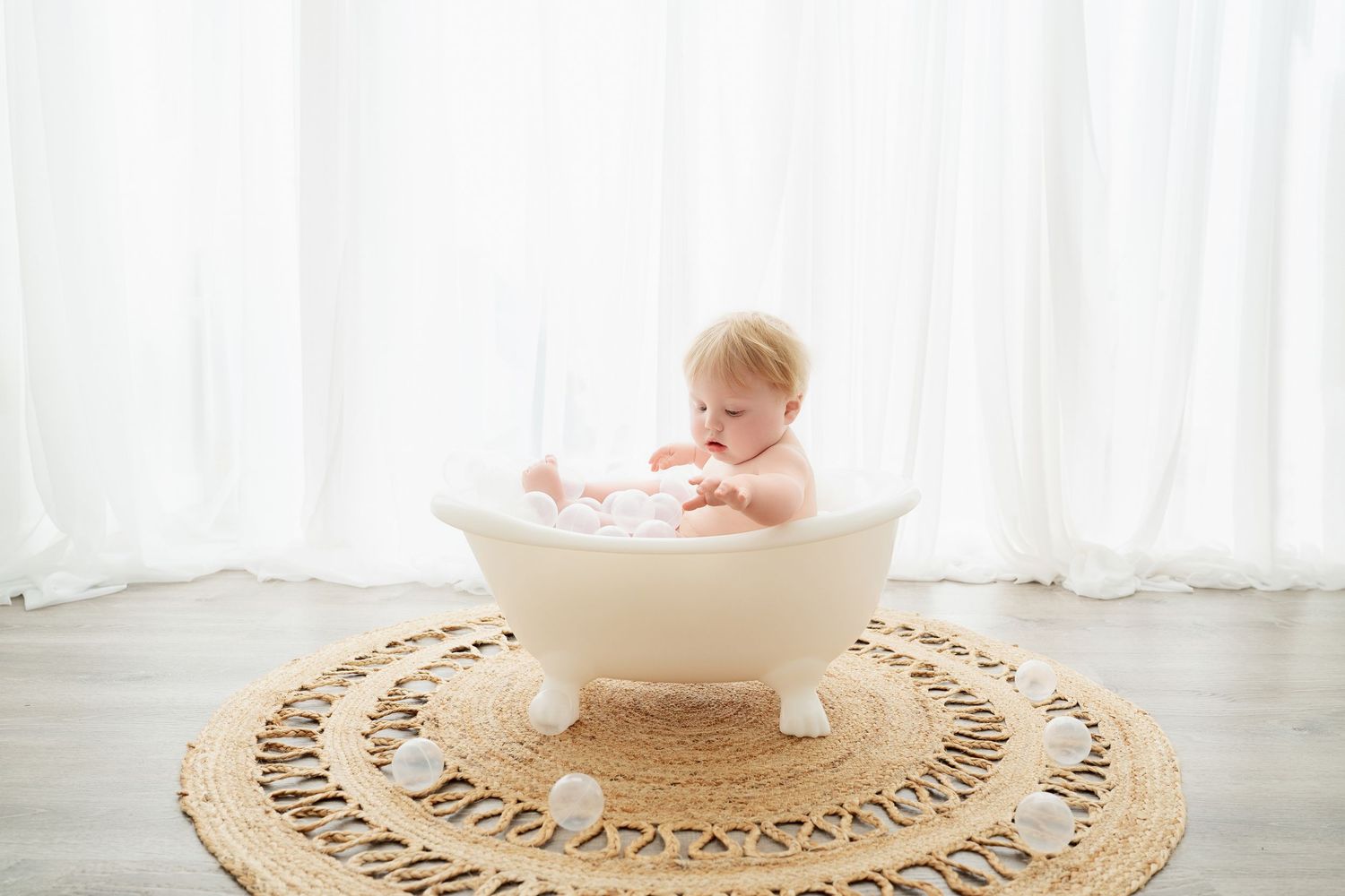 Central MN Milestone Photography - Cute baby sitting in small white bathtub on round jute rug.