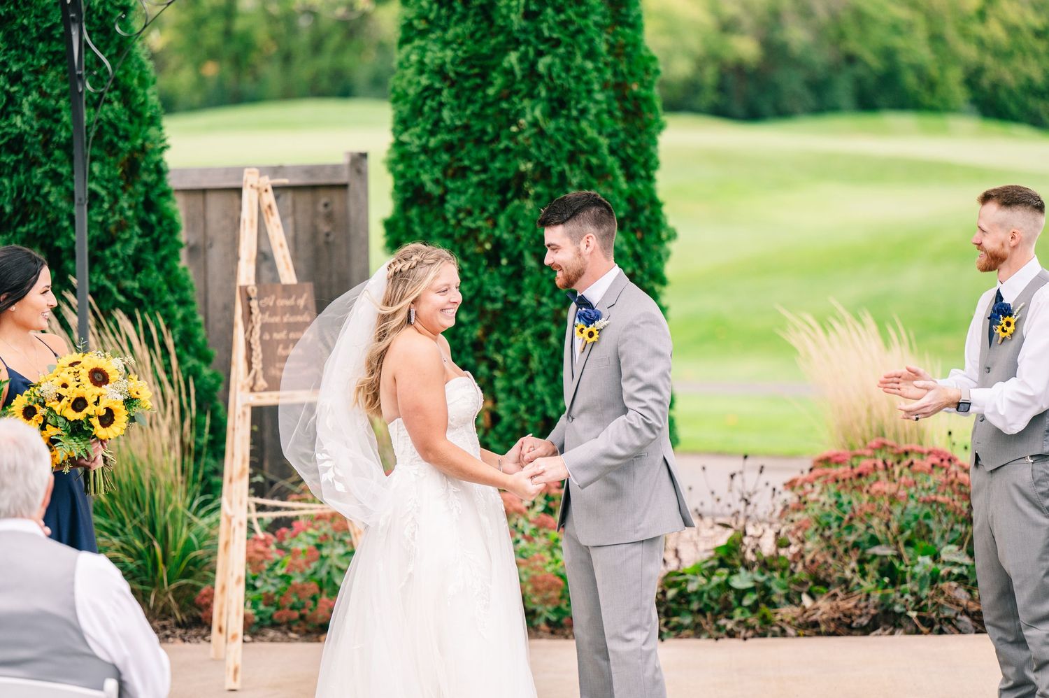 Central MN Wedding Photos - Bride and groom hold hands and smile during their outdoor wedding ceremony on a sunny fall day.