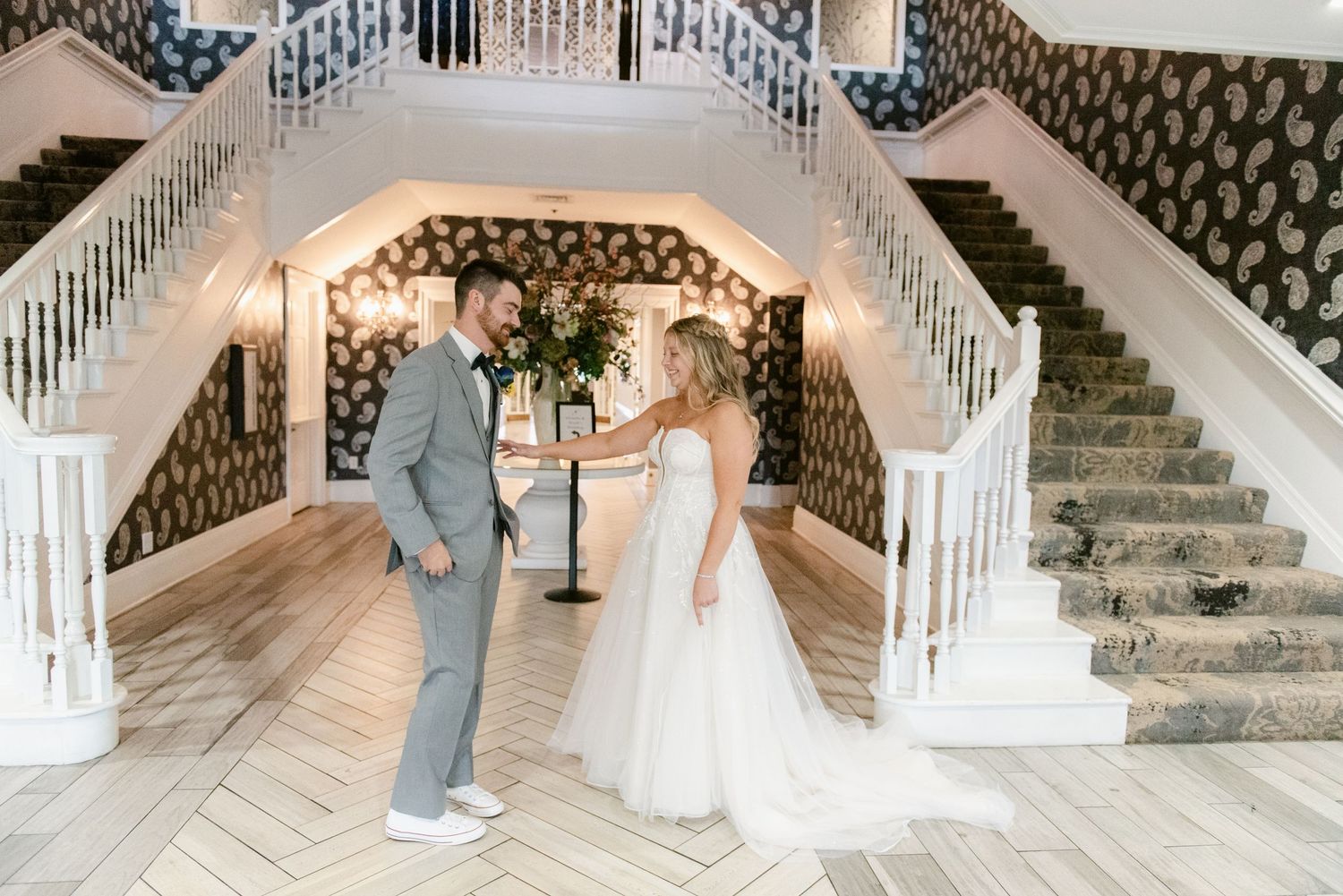 Central MN Wedding Photos | Bride and groom share first look moment in elegant venue foyer with grand white staircase.