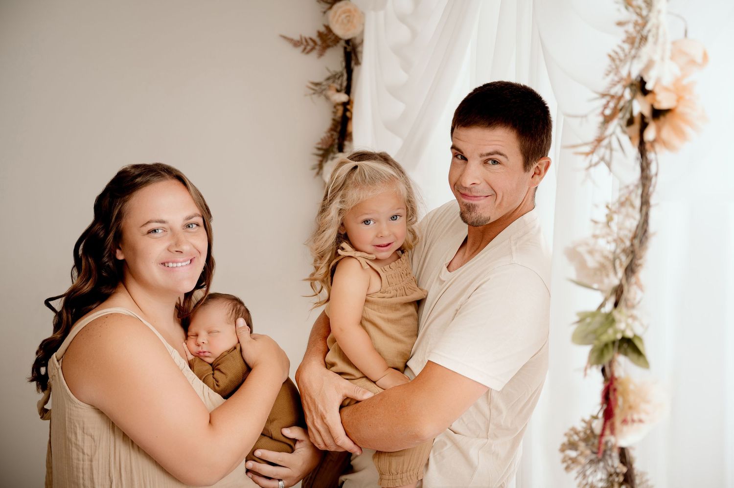Indoor family portrait with neutral tones and floral decorations against white backdrop.