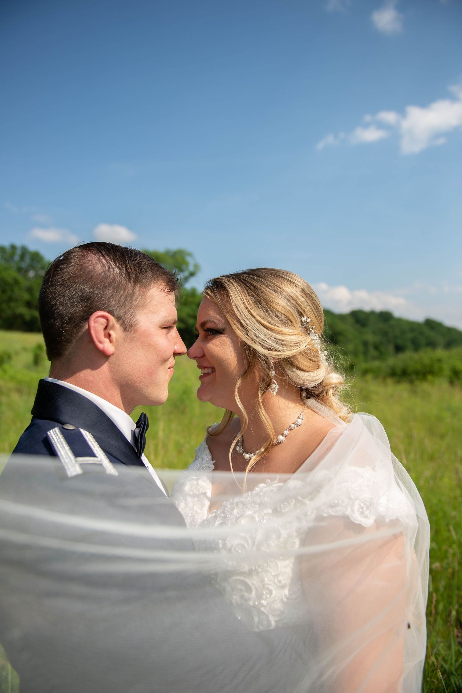 A romantic wedding portrait with flowing veil against blue sky and green field background. Zimmerman MN Weddings