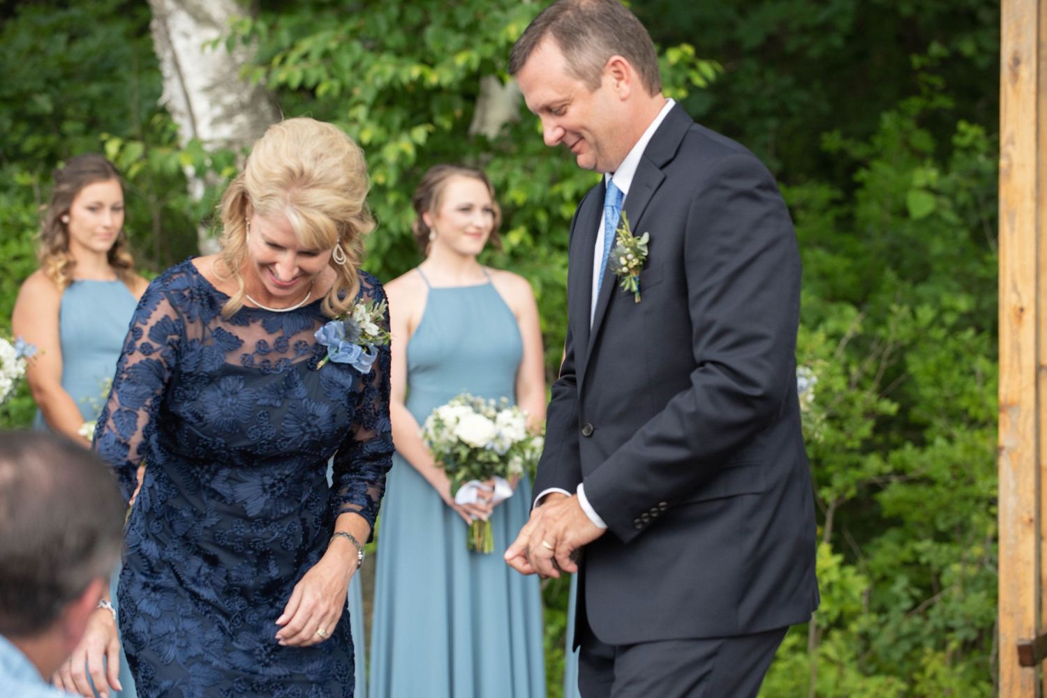 Wedding couple sharing a tender moment on their special day with bridesmaids wearing sage green dresses in background. Zimmerman MN Weddings