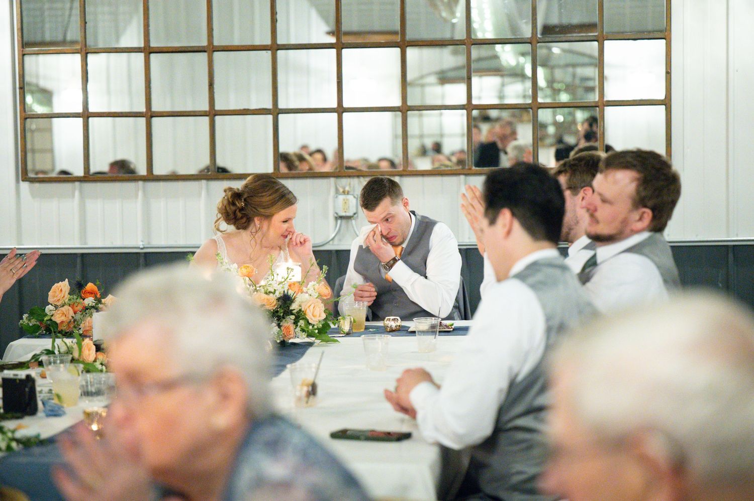 Bride and groom laugh together at sweetheart table during wedding reception dinner.