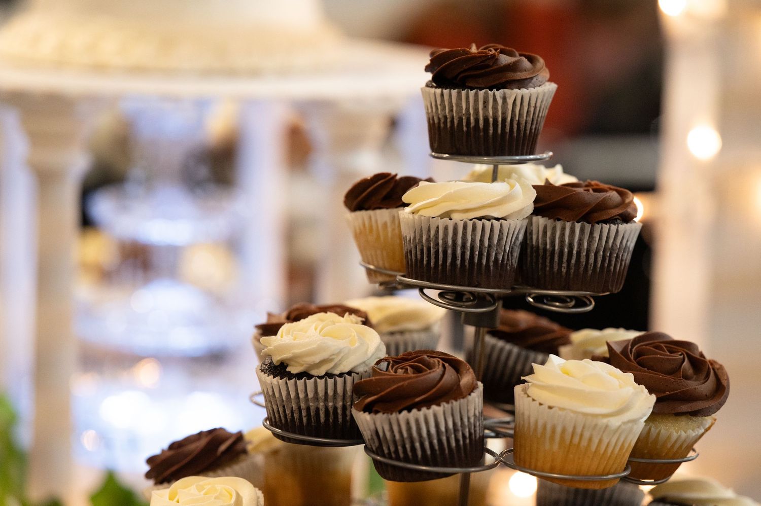 Chocolate and vanilla frosted cupcakes arranged on tiered display stands at a wedding reception.