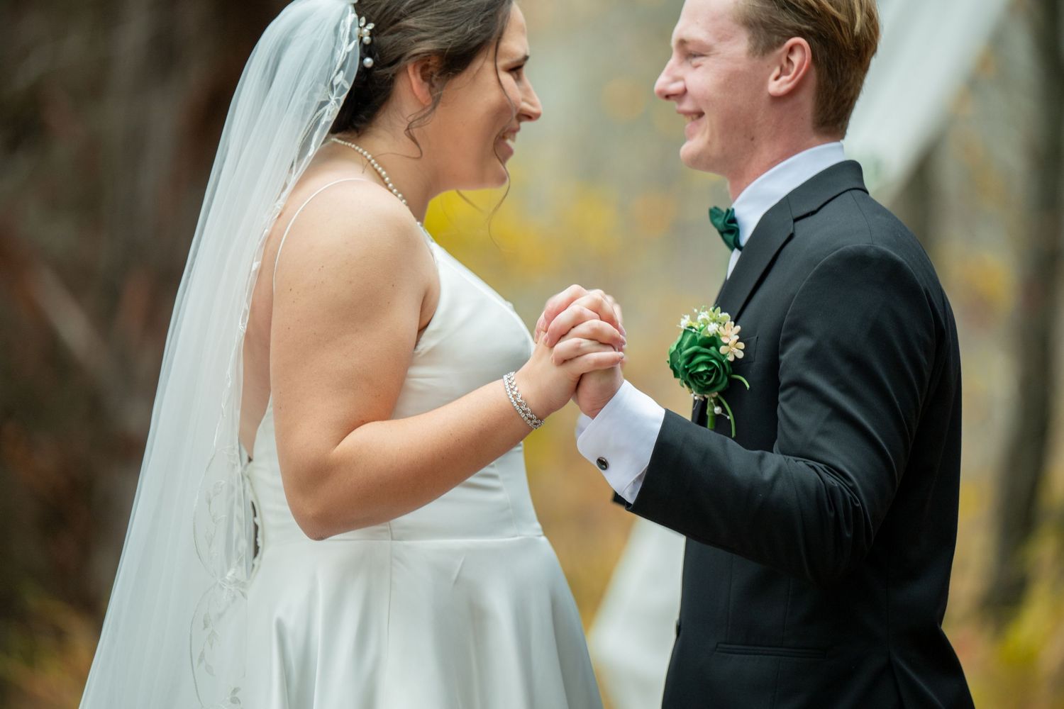 A bride and groom laugh together during their outdoor autumn wedding ceremony.
