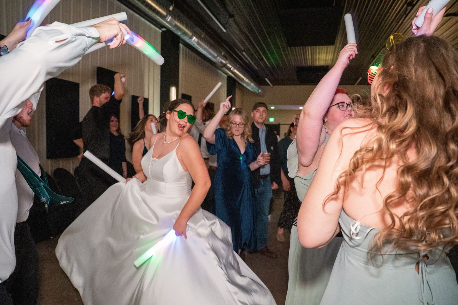 People dancing and celebrating on a dance floor at a wedding reception with colorful lighting effects.