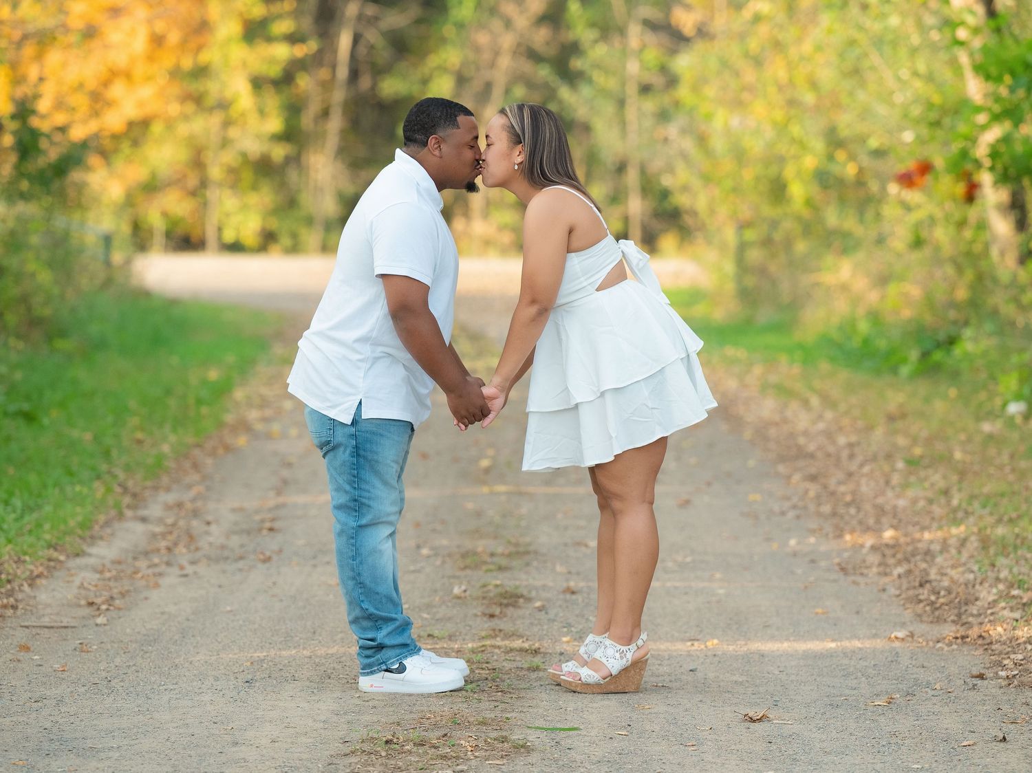A couple shares romantic moments on a tree-lined path during an autumn engagement photo session.