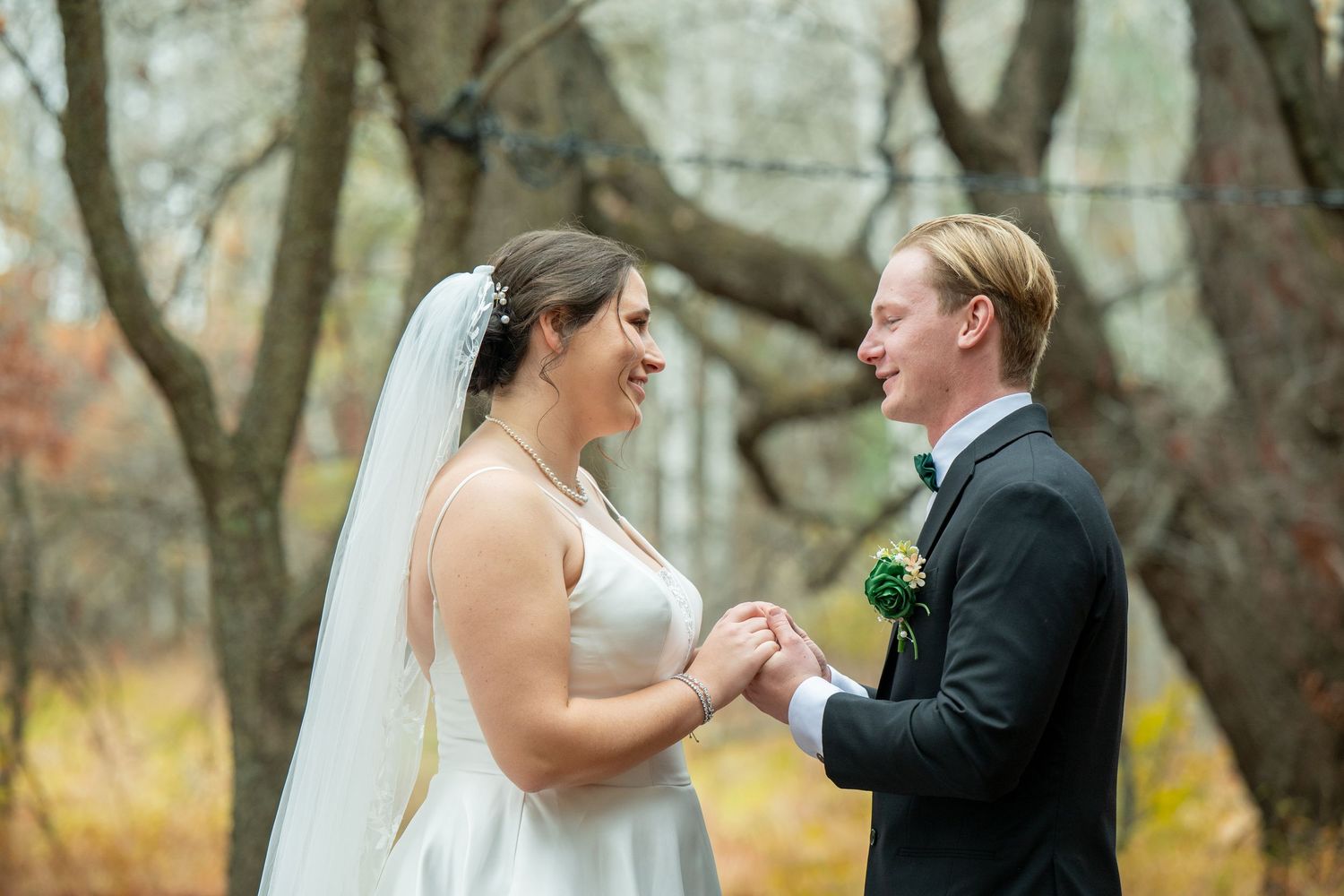 A joyful wedding couple shares a candid moment together outdoors in an autumn forest setting.