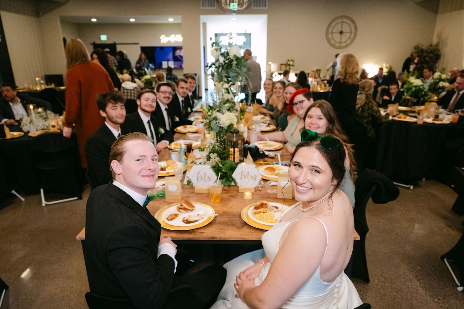 Wedding reception guests enjoying dinner at tables in modern venue setting.