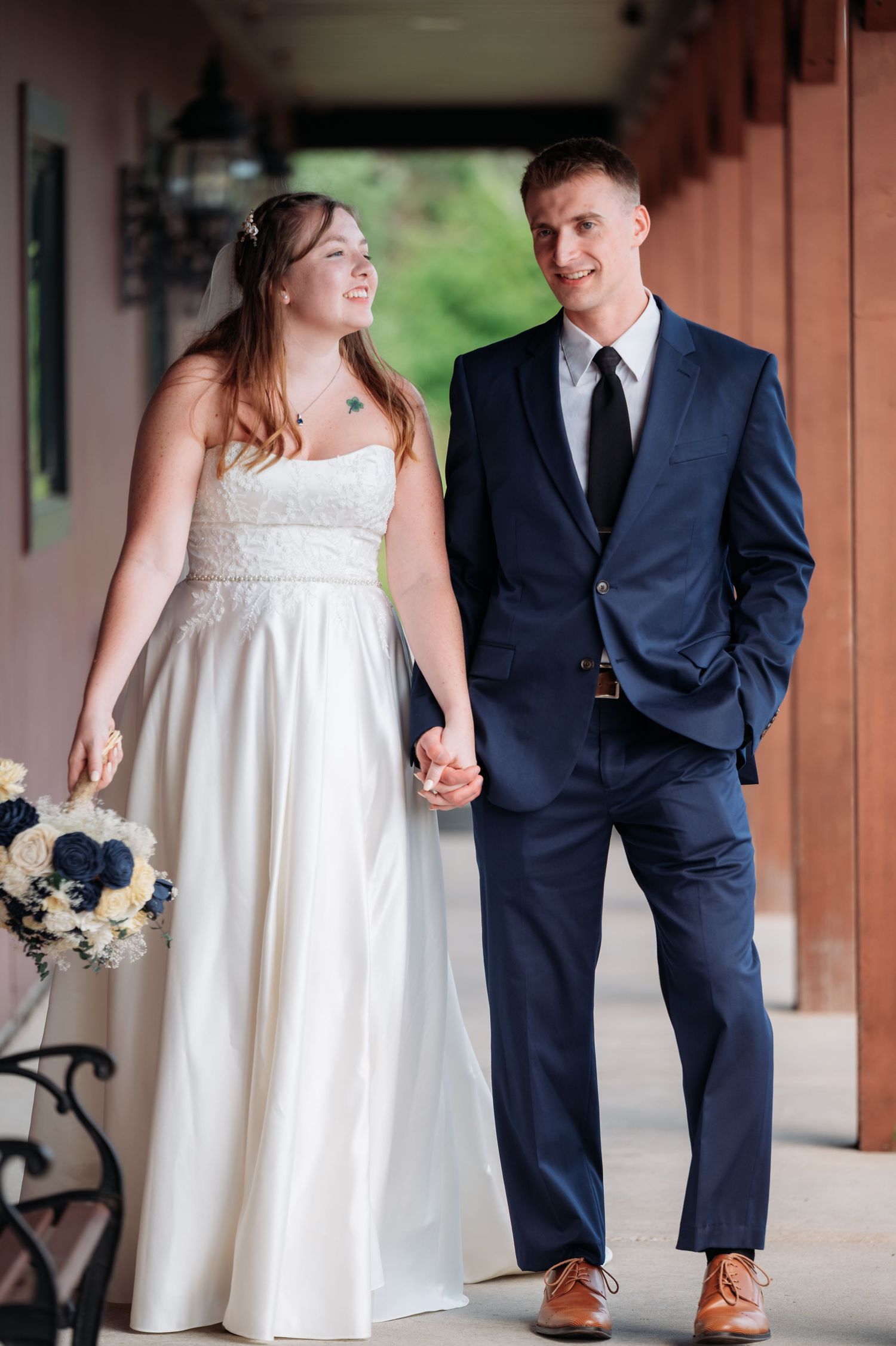A couple in wedding attire walking and holding hands along a covered walkway at Northern Lights near Milaca MN..