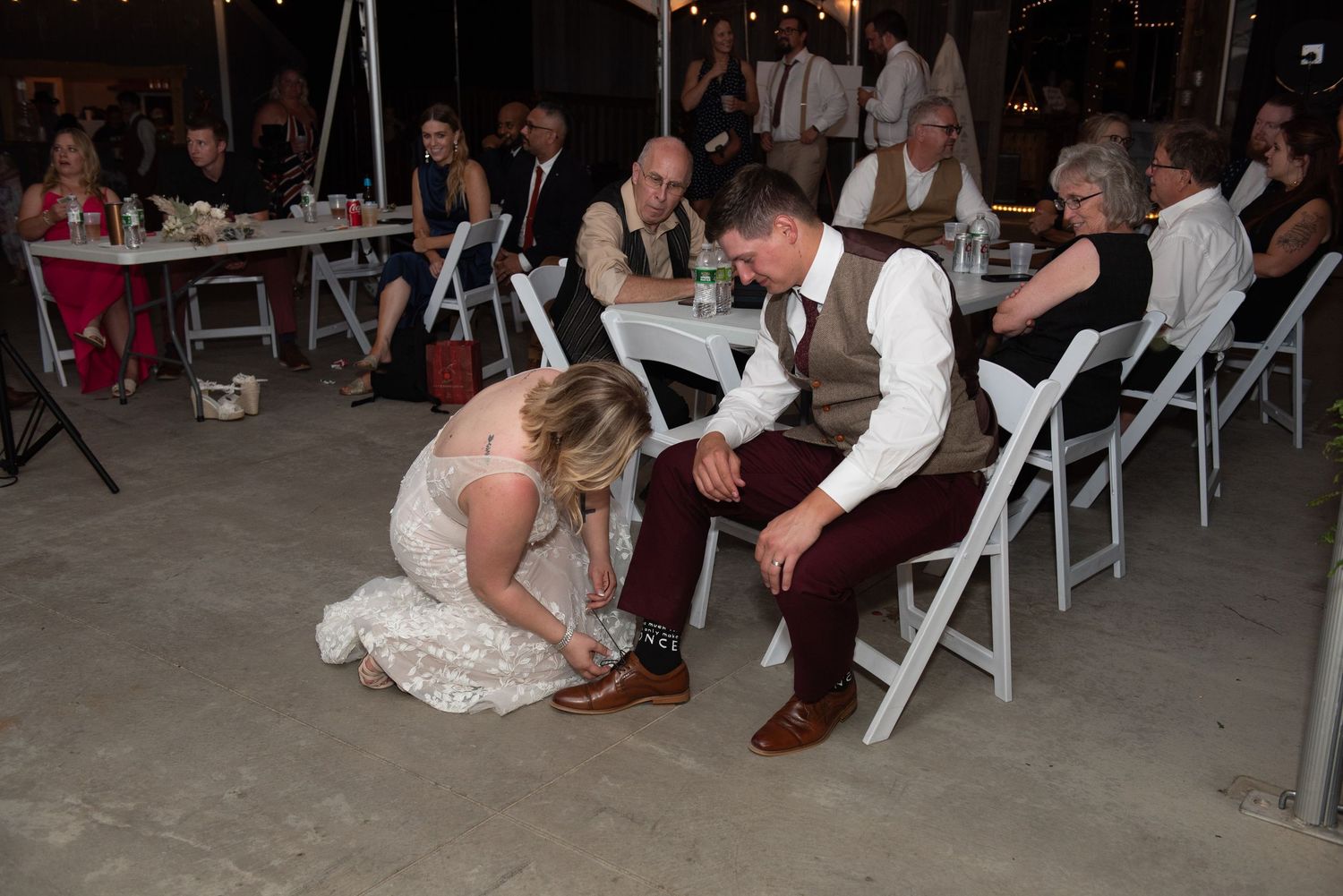 Wedding reception guests dancing in a rustic barn venue with folding chairs.