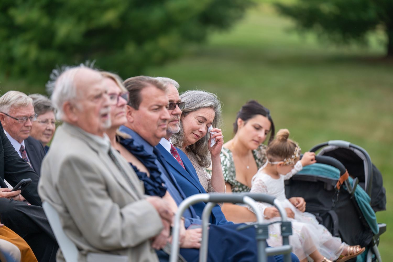 Wedding guests seated in white chairs watch an outdoor ceremony.