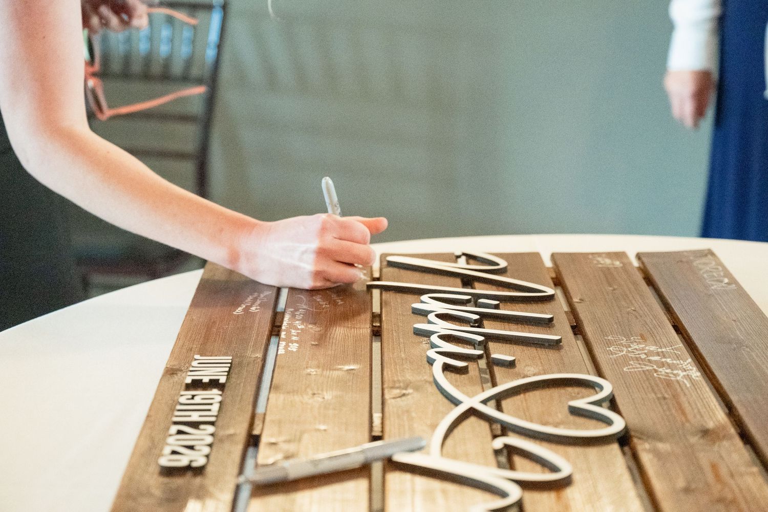 Guest signing a rustic wooden wedding guest book with decorative laser-cut lettering at reception.