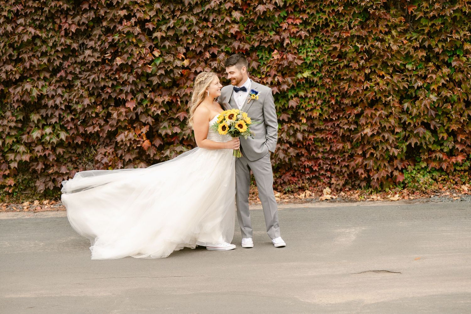 Central MN Wedding Photos | Bride and groom share a joyful moment in front of colorful autumn ivy wall outdoors.