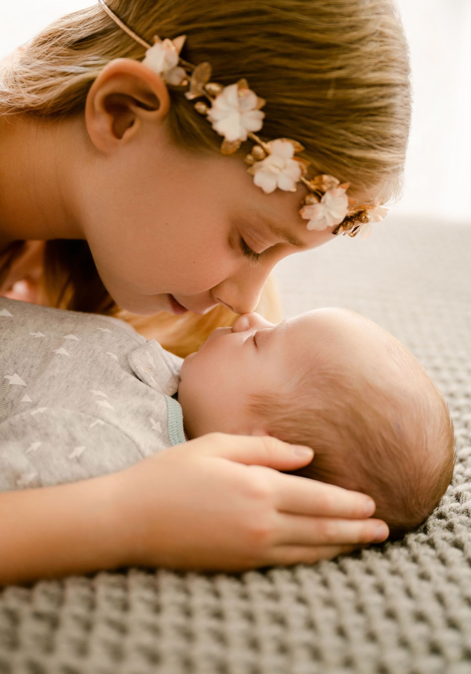 St Cloud newborn Photography of a Young girl with flower crown kissing sleeping newborn baby.