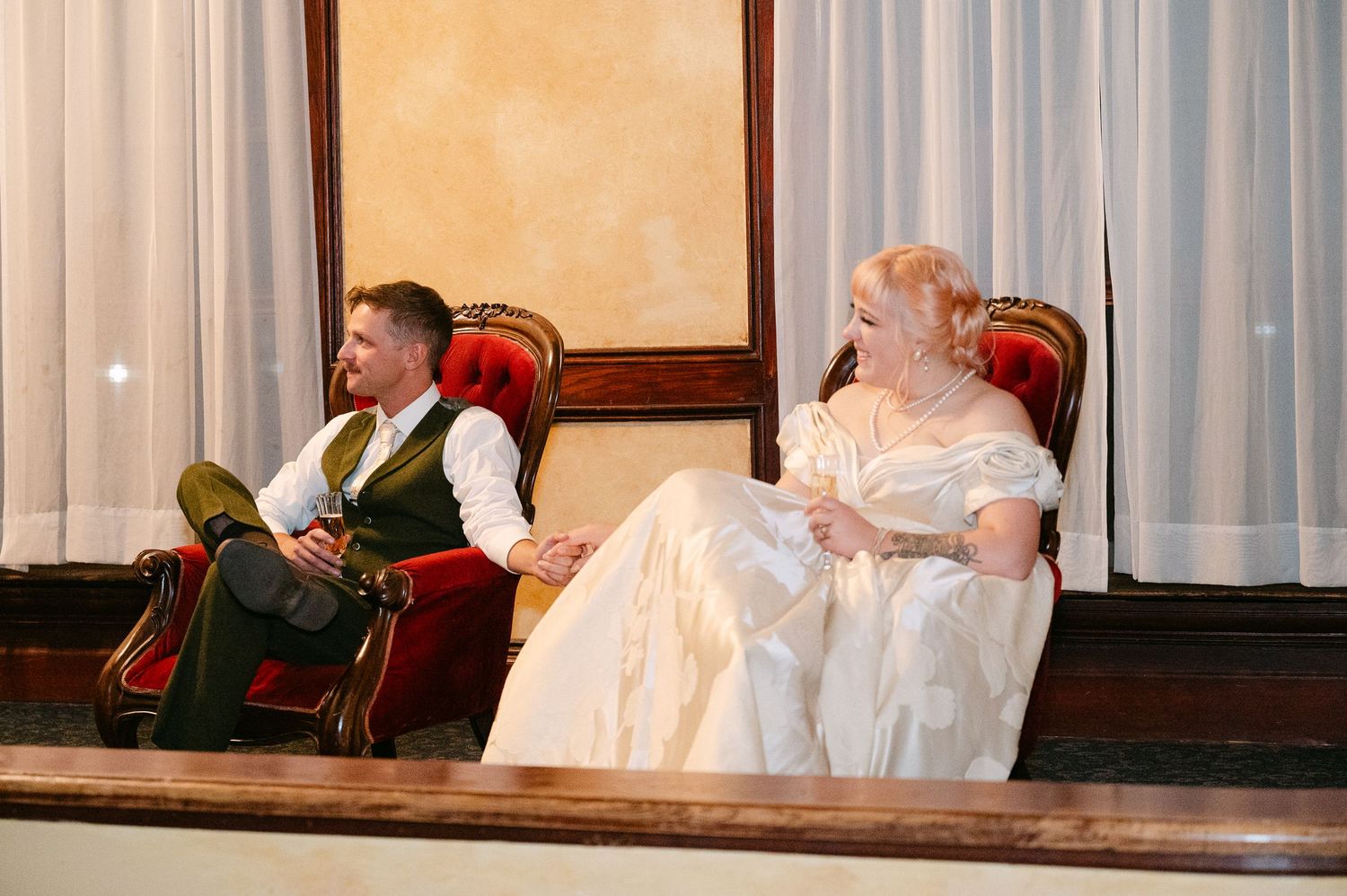 Central MN Wedding Photos | Man and woman in Victorian period costumes seated in ornate red chairs during a theatrical performance.