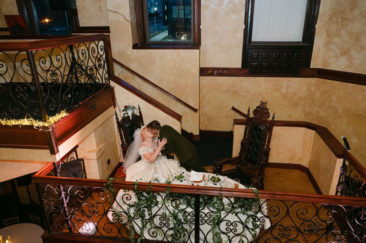Central MN Wedding Photos | Bride and groom sharing a kiss on ornate wrought iron staircase landing at wedding reception.