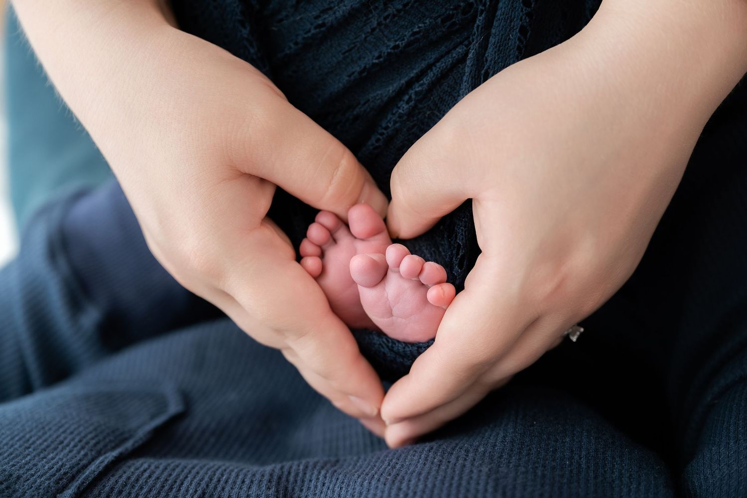 Minnesota Best newborn photographer -  a Close-up shots of tiny baby feet being gently held by adult hands against a dark background.