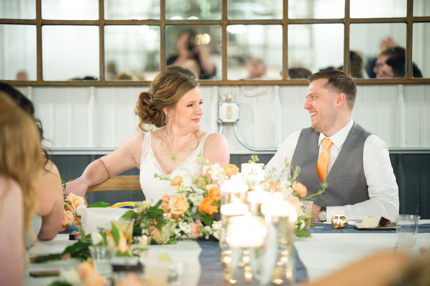 Bride and groom share a loving glance at their elegantly decorated wedding reception table.
