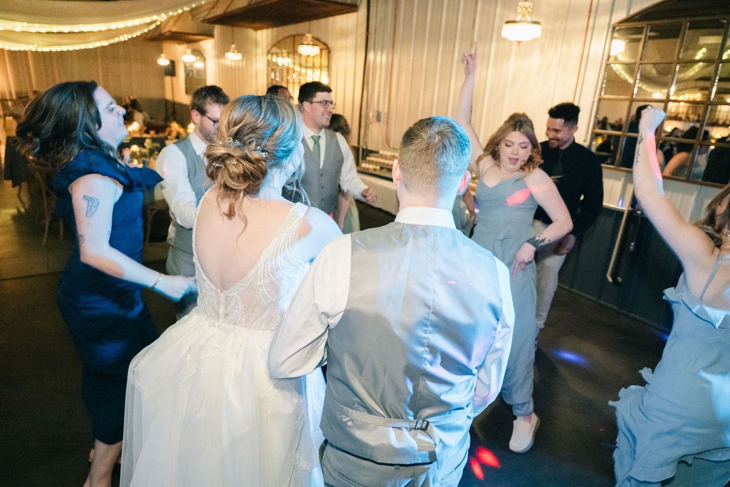 Bride and groom dance with guests on the lively wedding reception dance floor.
