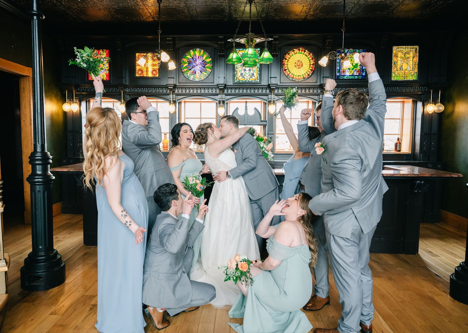 crooked willow weddings A wedding party celebrates the newlyweds with cheers inside a rustic venue with stained glass windows.