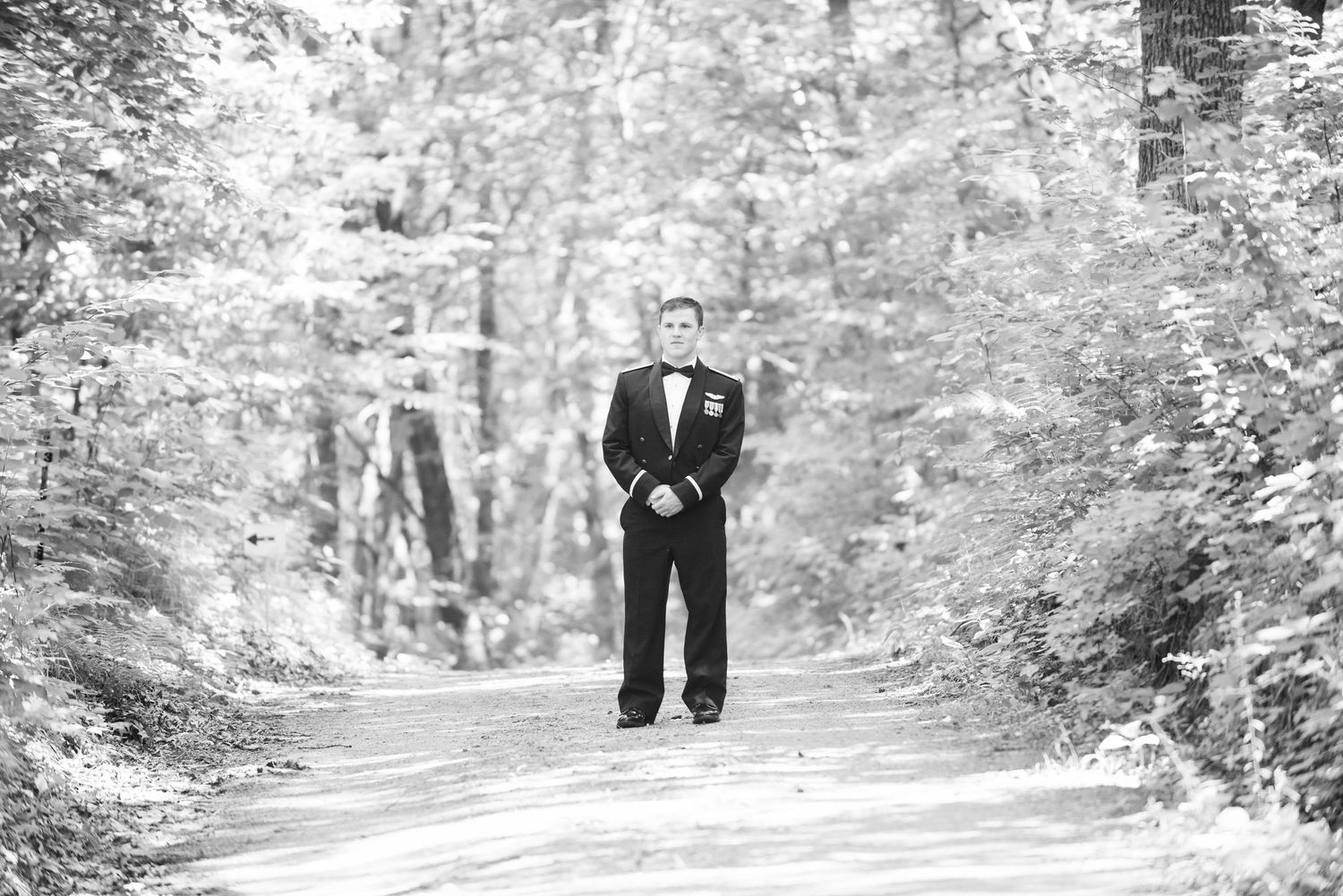 Black and white photo of person in formal attire standing on wooded path. Zimmerman MN Weddings