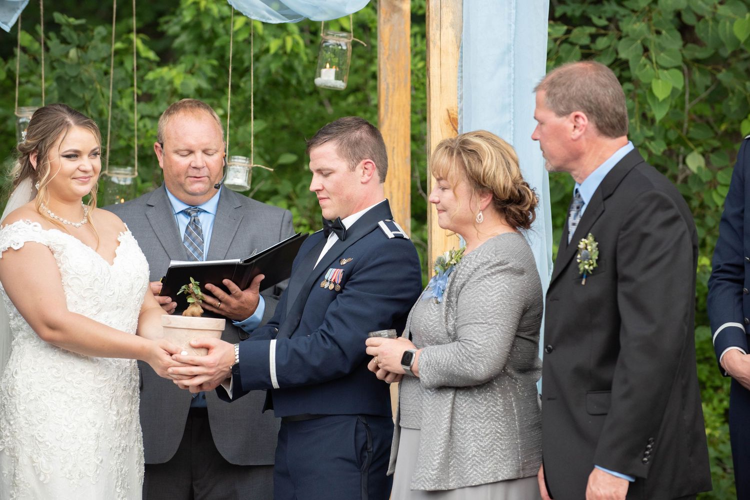 Wedding ceremony moment under wooden posts with flowing white fabric and green forest backdrop. Zimmerman MN Weddings