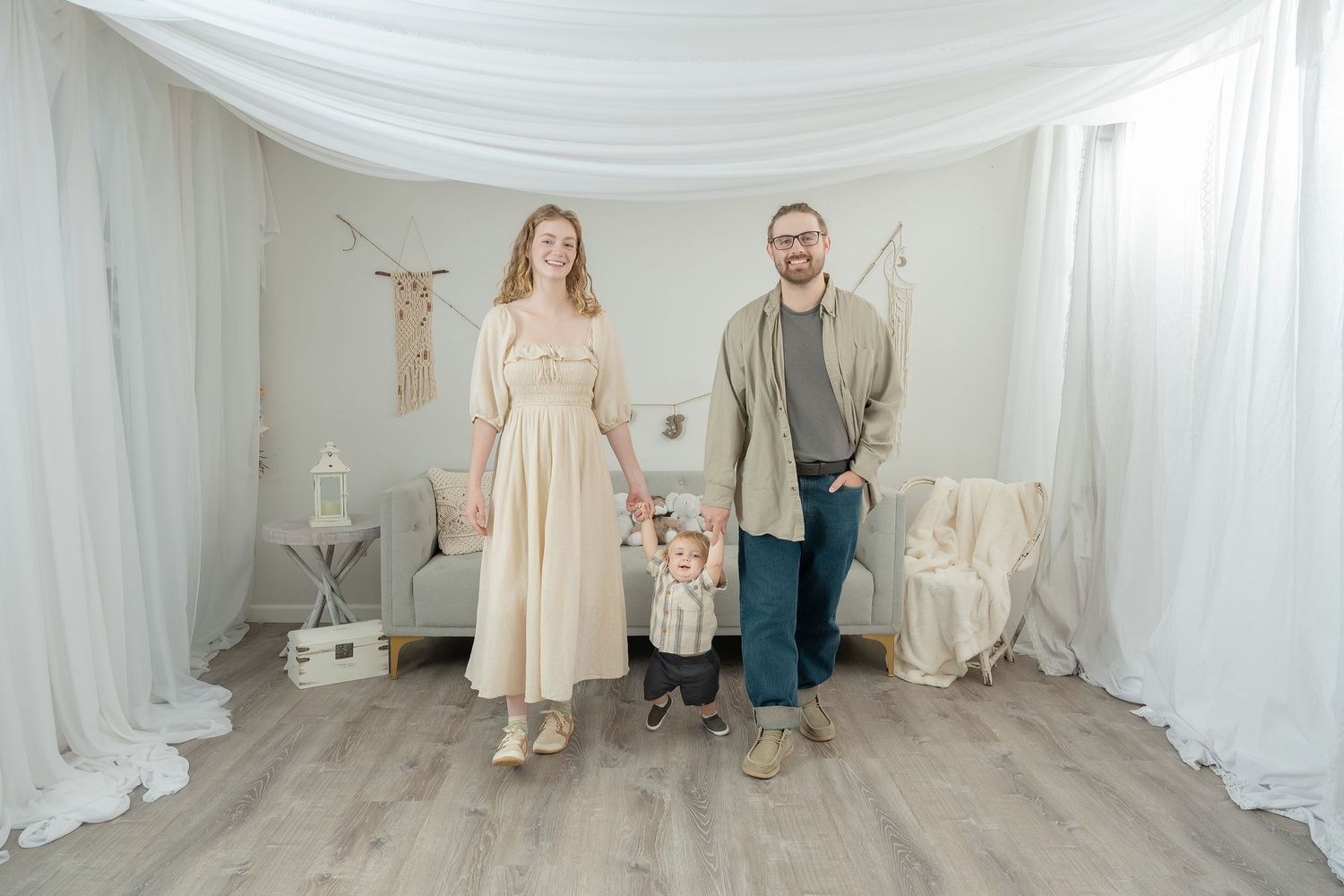 A small group poses in front of white draped backdrop in a rustic indoor setting. Princeton MN Milestone, Maternity and Newborn Photos