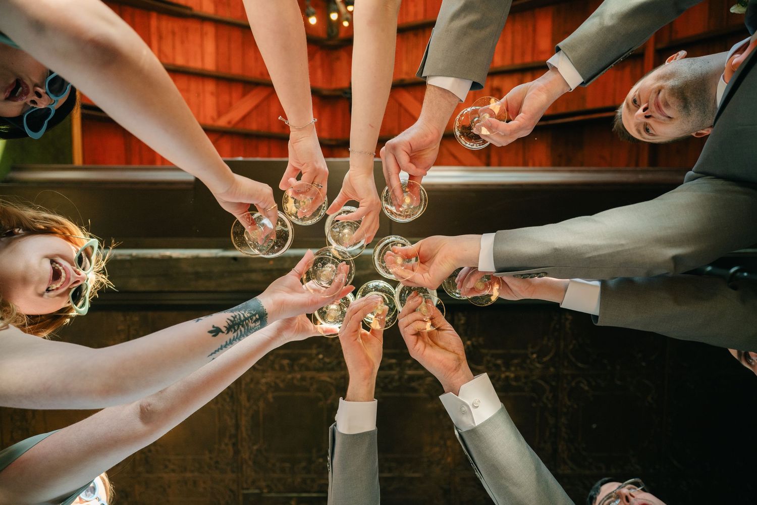 Group of friends toasting with champagne glasses in a circle, viewed from below at a wedding celebration.