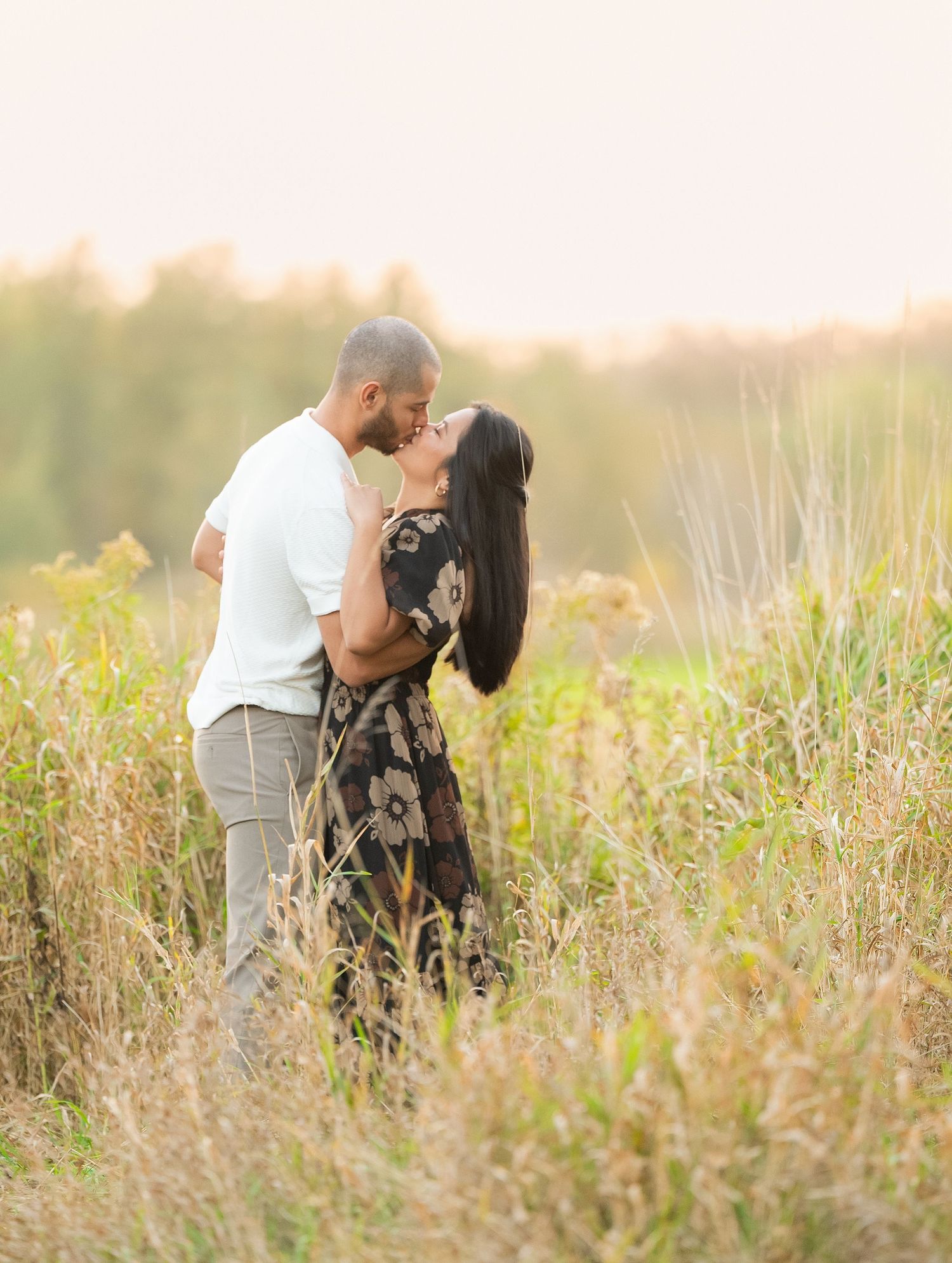 Central MN Engagement Session. A couple embraces lovingly among tall grasses in a golden meadow at sunset.