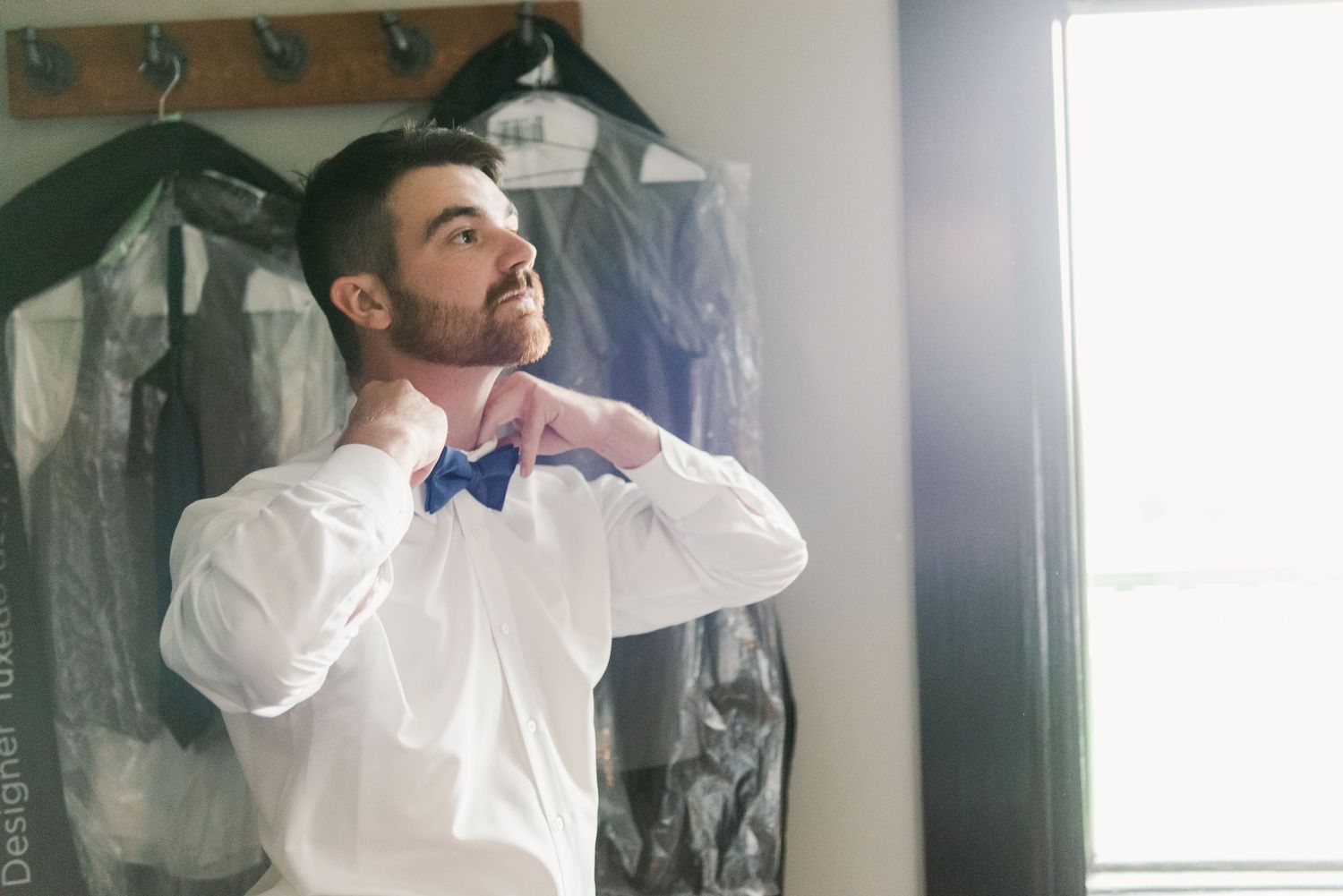 Central MN Wedding Photos | Groom adjusting blue bow tie in white dress shirt before wedding ceremony.