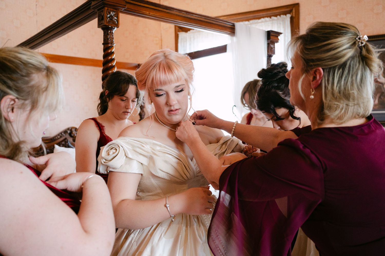 Central MN Wedding Photos | Bridesmaids help blonde bride into her off-shoulder wedding gown before ceremony.