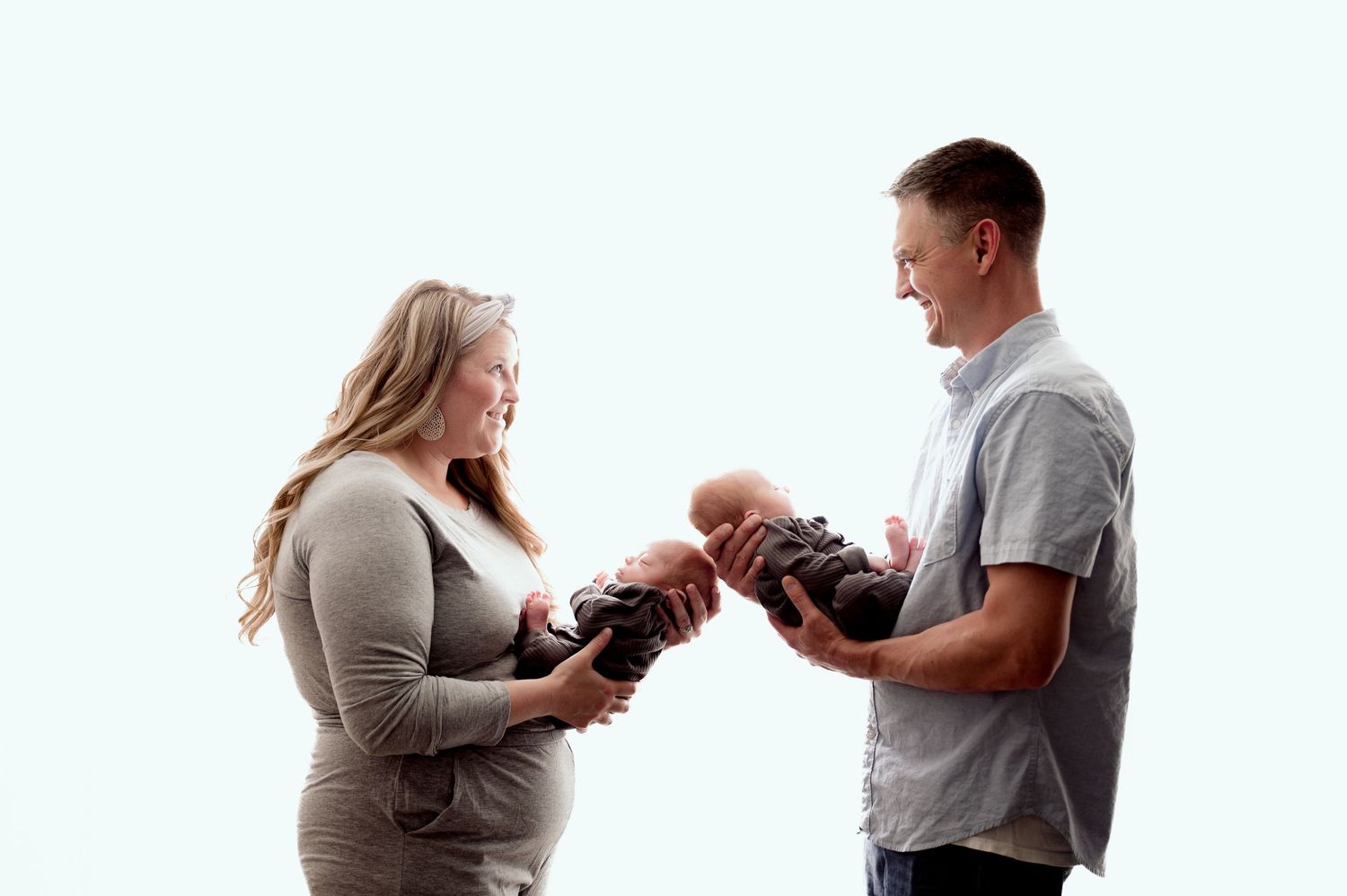 St Cloud newborn Photos of Expecting couple smiling at newborn baby held between them against a light blue background.