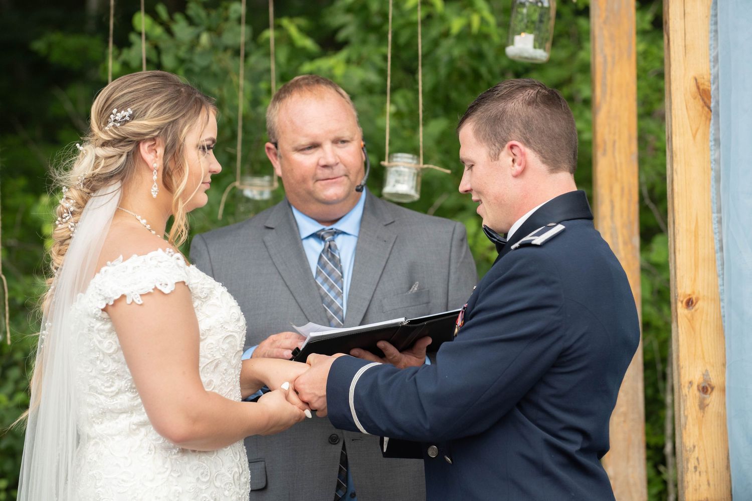 Wedding ceremony taking place under rustic wooden pergola with greenery backdrop. Zimmerman MN Weddings