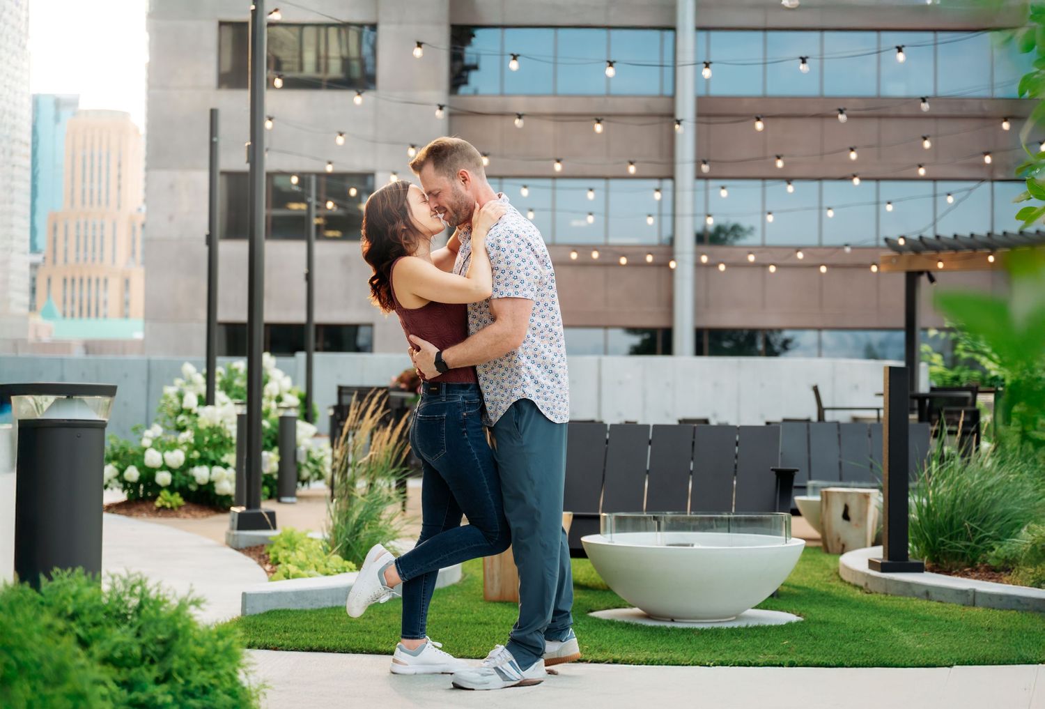 A couple embraces in a romantic outdoor setting with string lights and greenery providing a dreamy ambiance.