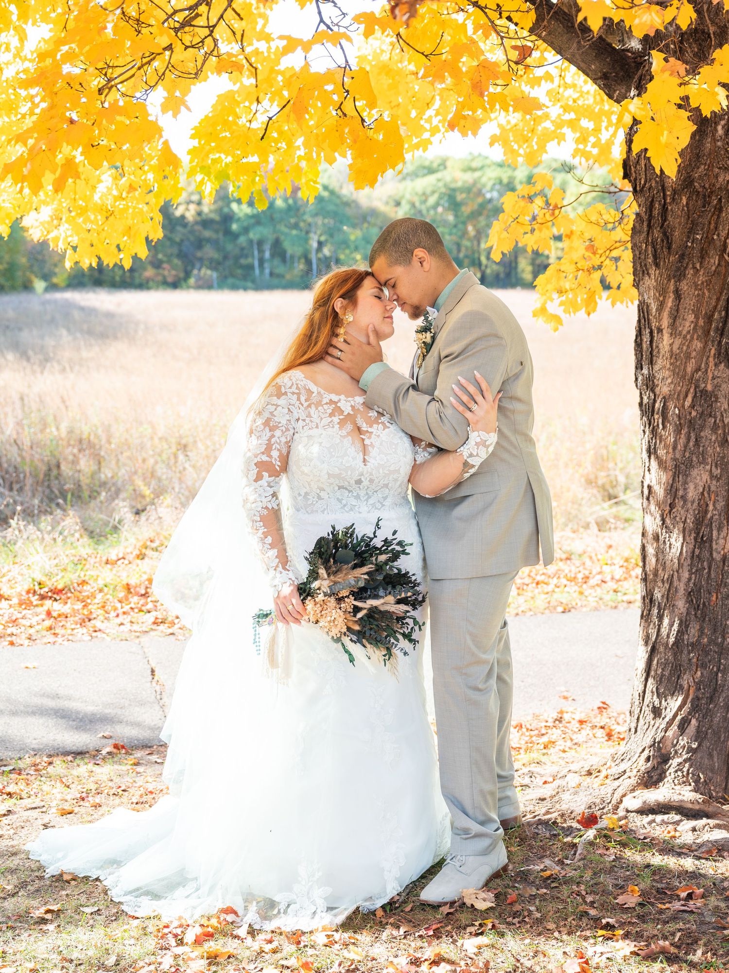 Bride and groom share a romantic moment under a vibrant yellow maple tree surrounded by fall foliage.