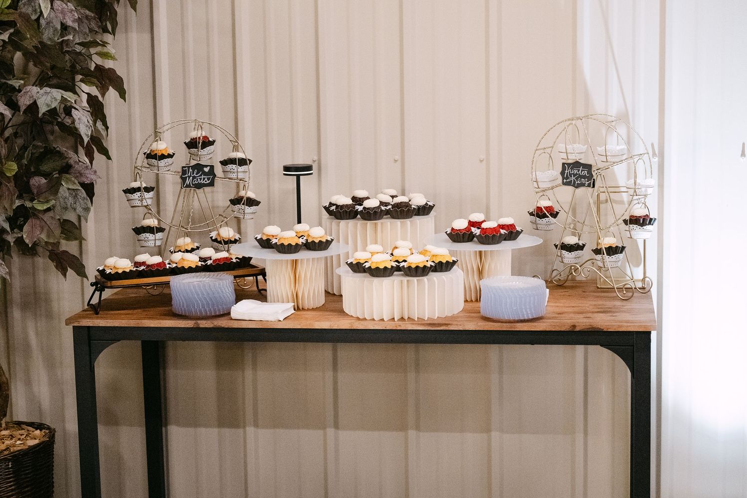 A rustic wooden dessert table displays an elegant arrangement of cupcakes and sweets at a wedding reception.