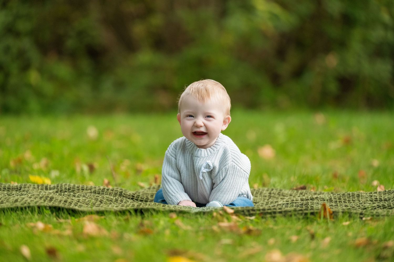 A joyful child lies on green grass in a garden setting during a sunny outdoor photo session.
