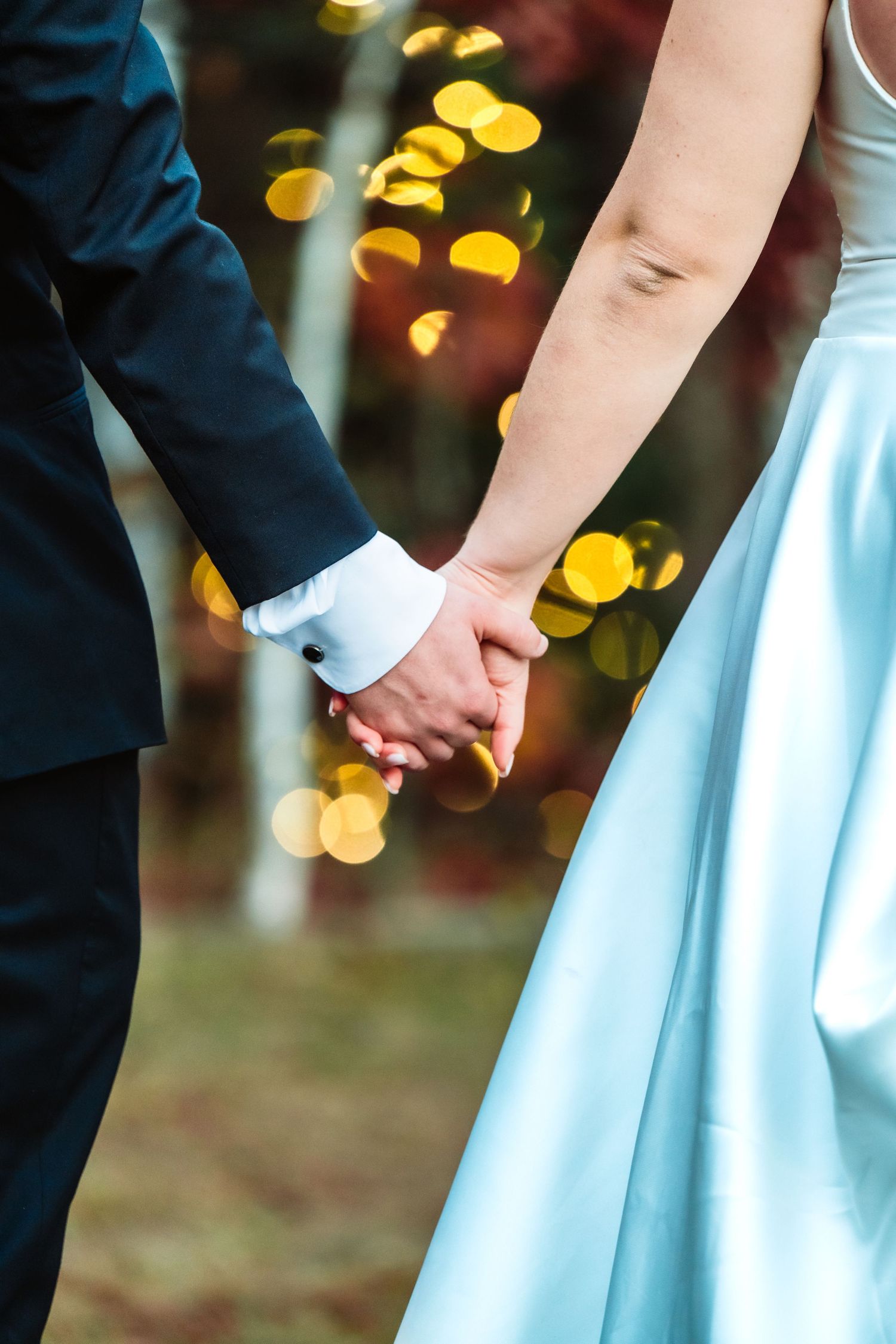 Close-up of joined hands against a backdrop of soft bokeh lights at dusk.