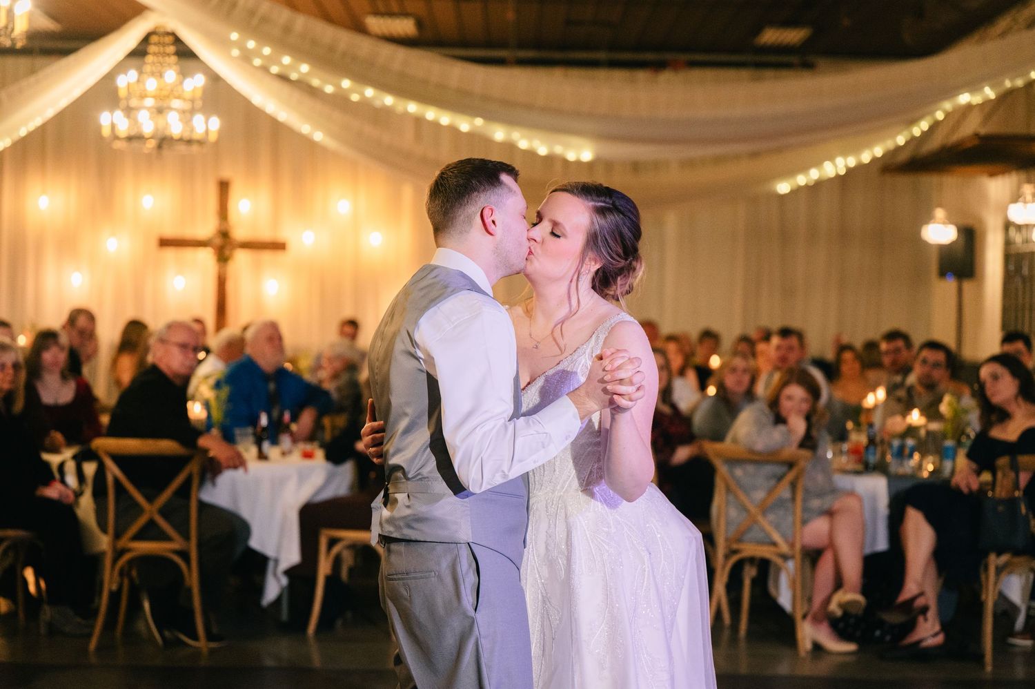 Bride and groom share their first dance kiss under warm lights at their wedding reception.