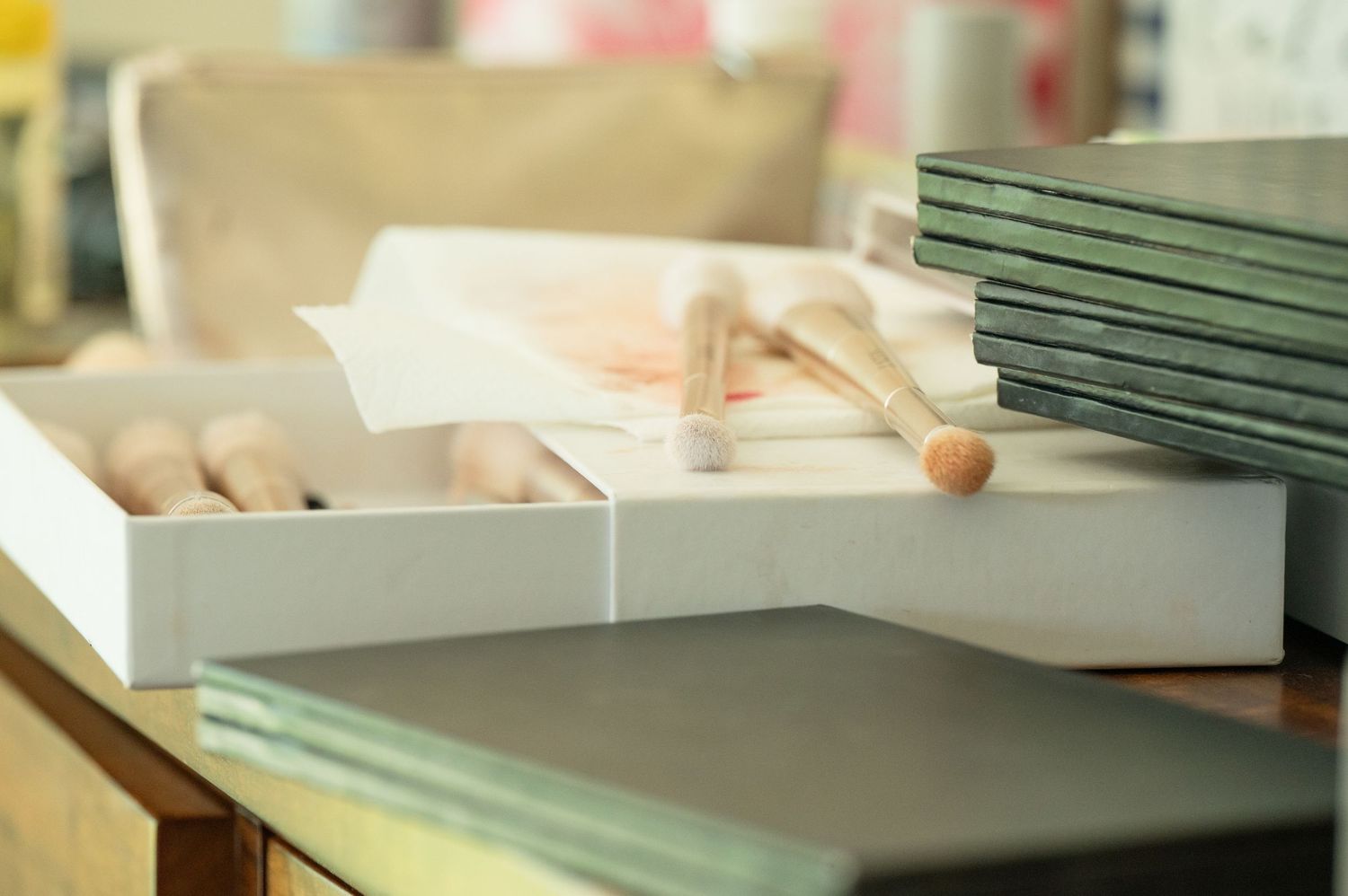 Stack of green hardcover books beside a white box with wooden craft tools on a wooden table.
