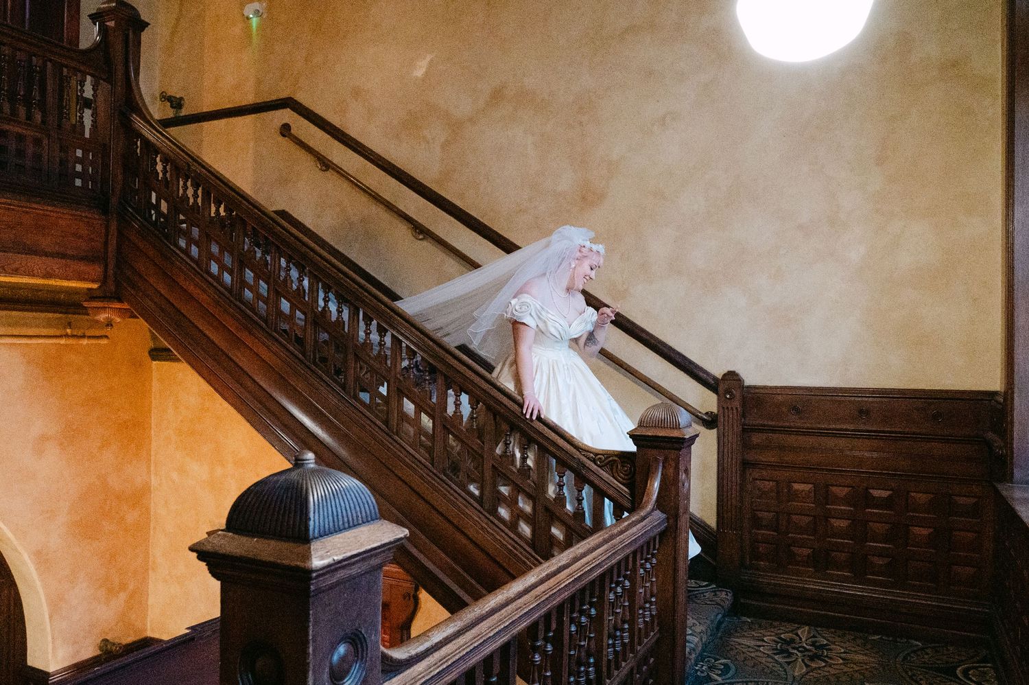 Central MN Wedding Photos | Bride in white wedding dress and veil descending elegant wooden staircase in historic venue.