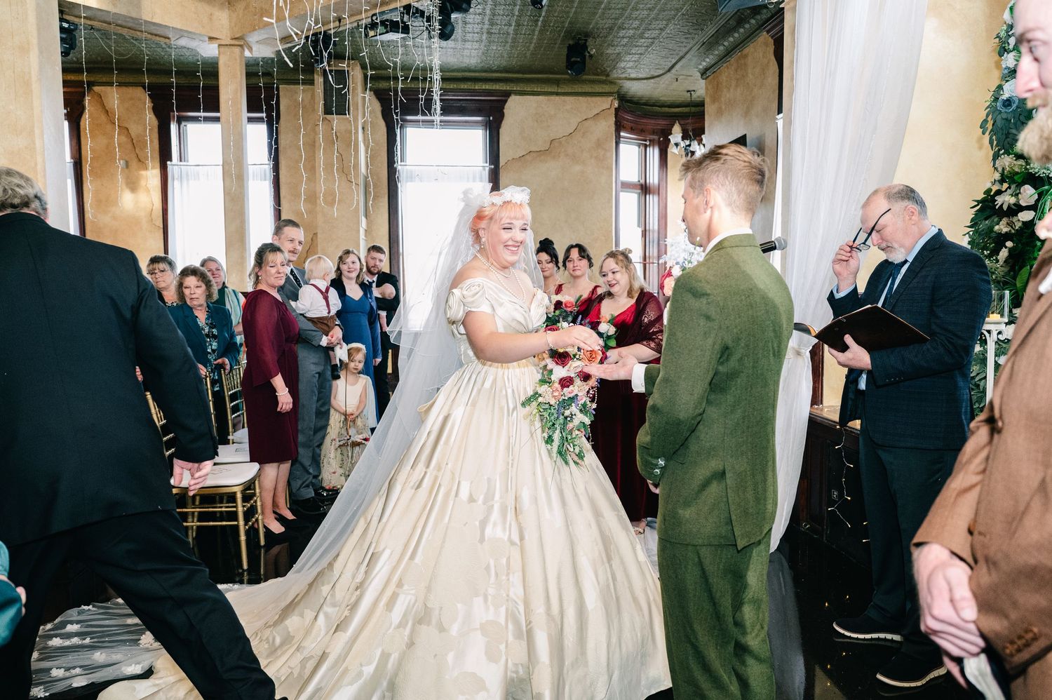 Central MN Wedding Photos | Bride in ivory ballgown exchanges vows with groom in olive suit during elegant wedding ceremony with guests.