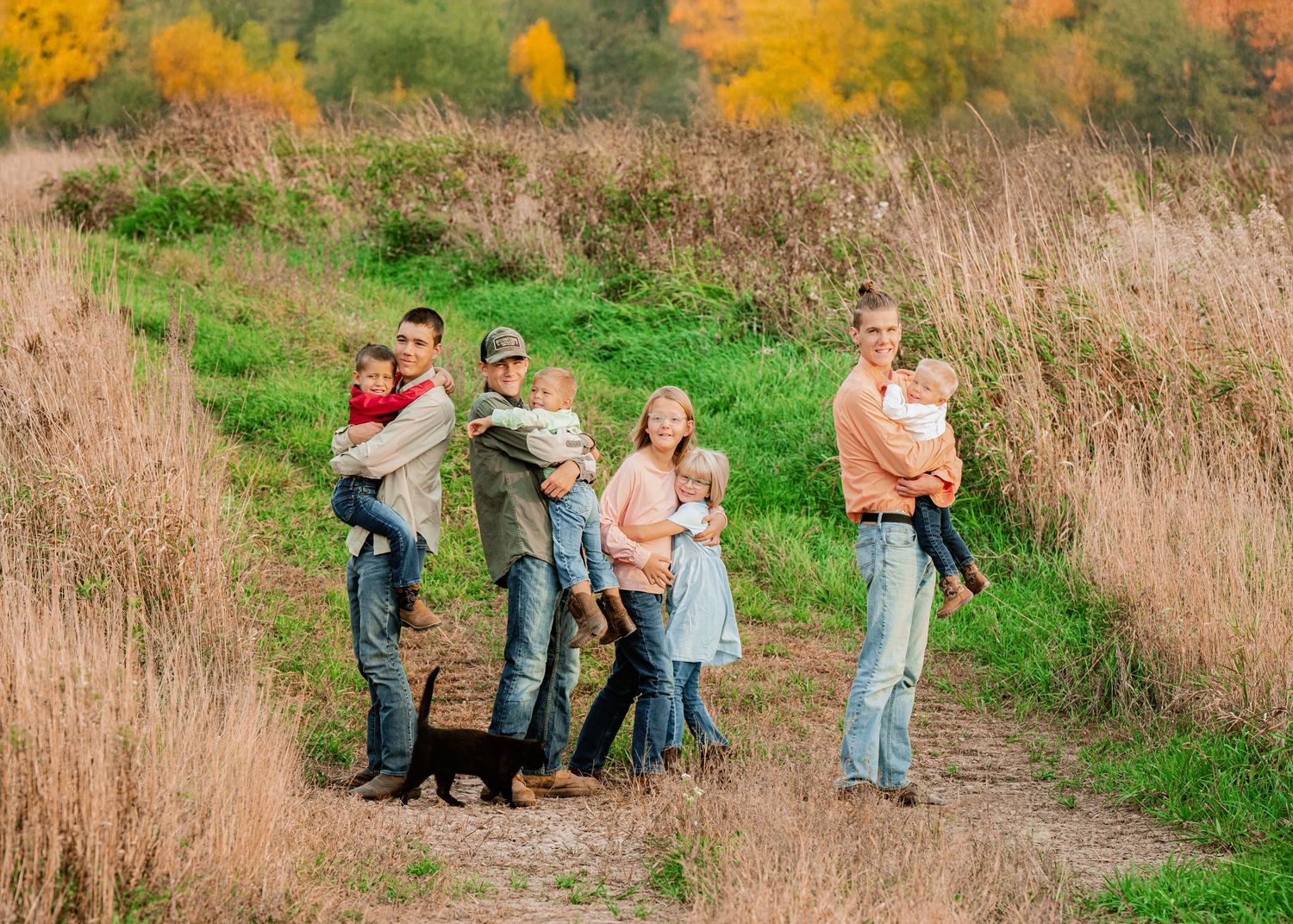 A family group walks along a grassy path with fall colors in the background.