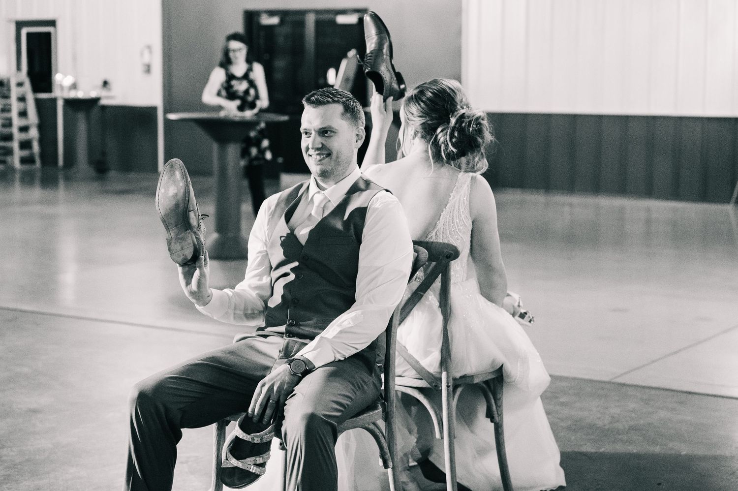 Black and white photo of groom laughing during the garter removal tradition at wedding reception.