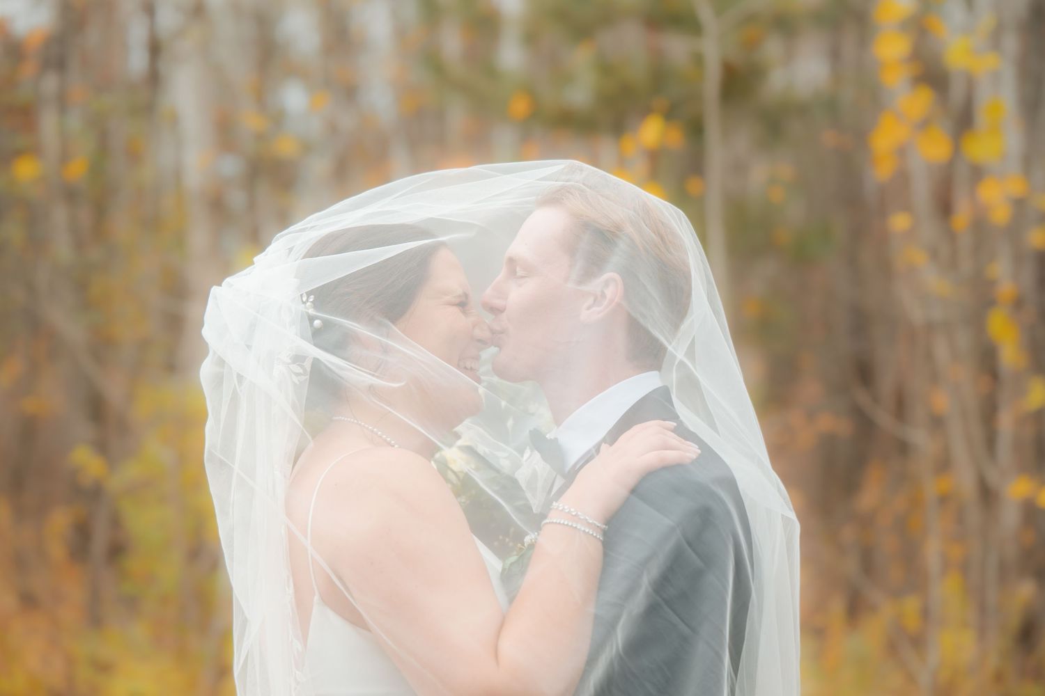 A romantic moment under a veil with fall foliage in the background.
