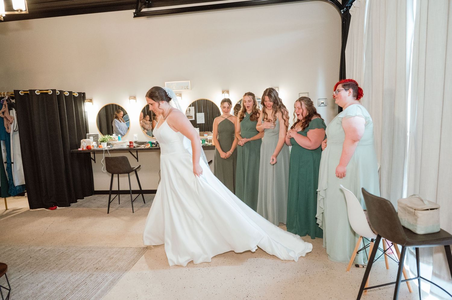 A wedding party dances and celebrates together in a bright reception venue with bridesmaids in green dresses.