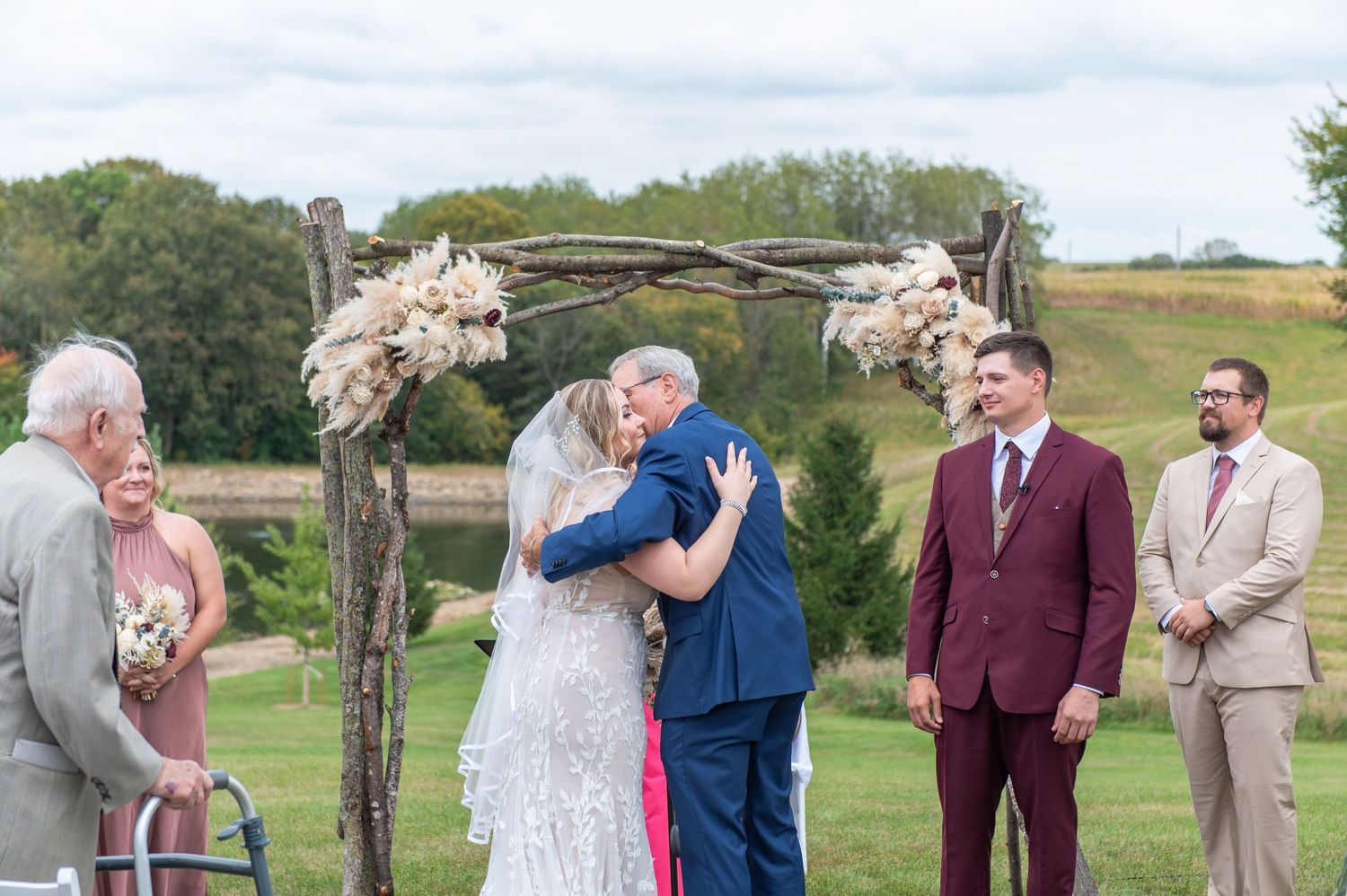 Outdoor wedding ceremony under rustic wooden arch decorated with dried flowers.